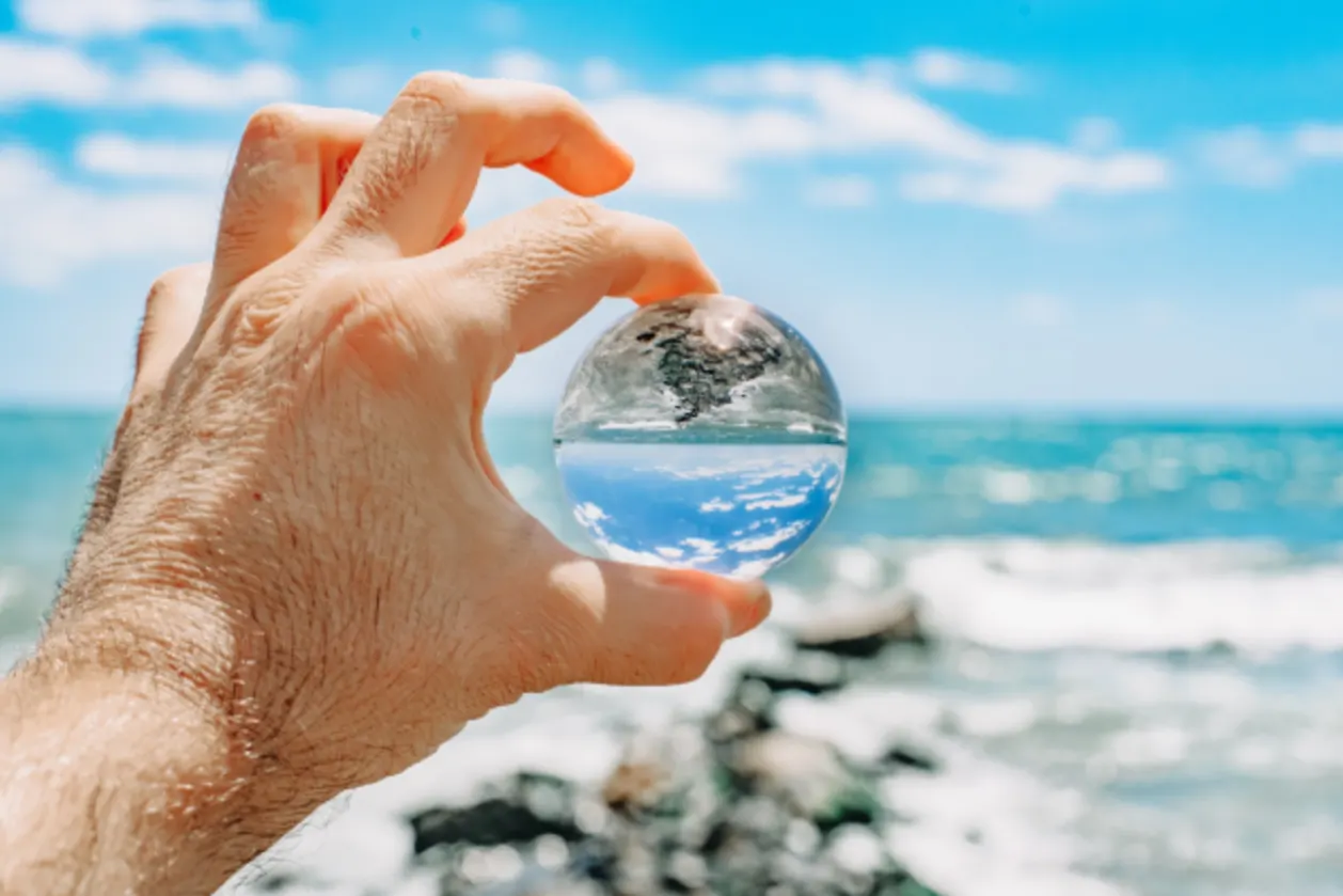 man-holding-seascape-reflecting-in-a-glass-ball-on-the-beach representing sustainable travel